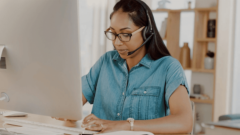 Person typing at a desktop computer while wearing a headset